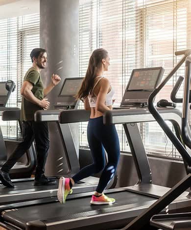 Woman and man on a treadmill in a gym.